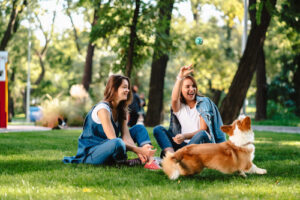 two young women playing with corgi dog at the park